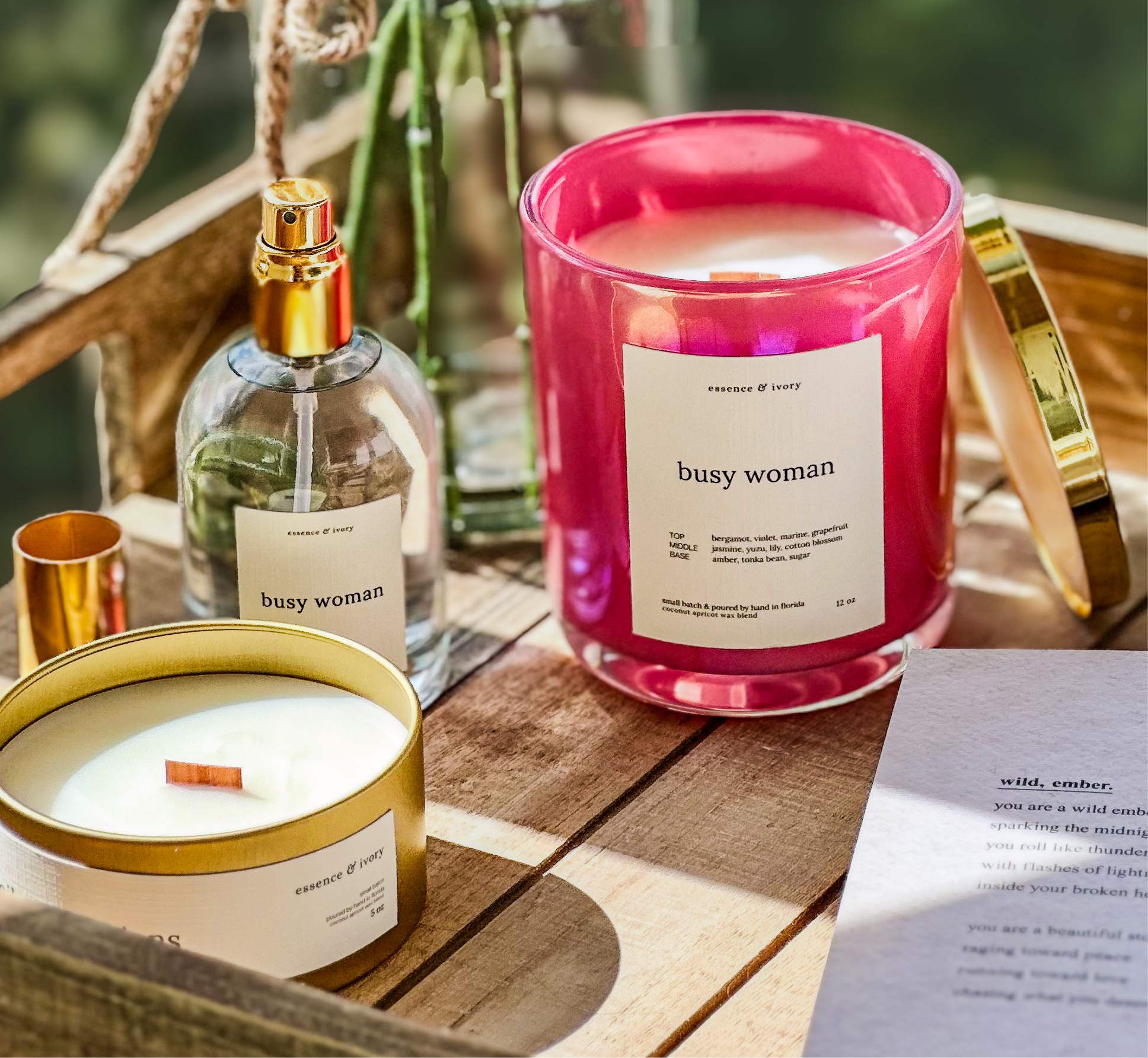 Two candles labeled 'busy woman' on a wooden surface with a bottle of perfume.