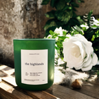 Green candle labeled 'the highlands' on a wooden surface with white flowers and greenery in the background