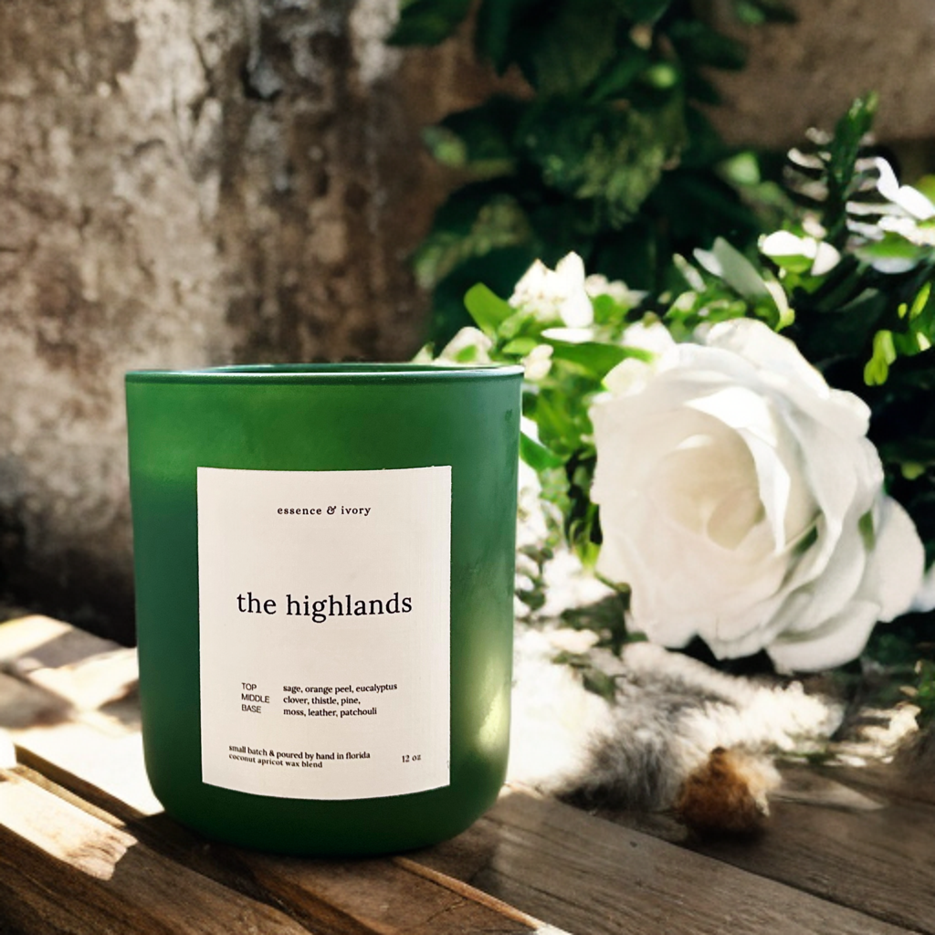 Green candle labeled 'the highlands' on a wooden surface with white flowers and greenery in the background